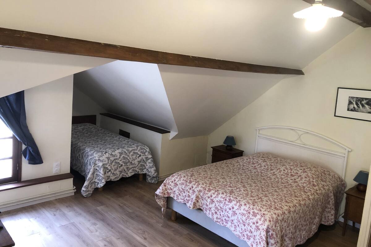 A bedroom with two beds, wooden beams, a ceiling fan, and a window with curtains.