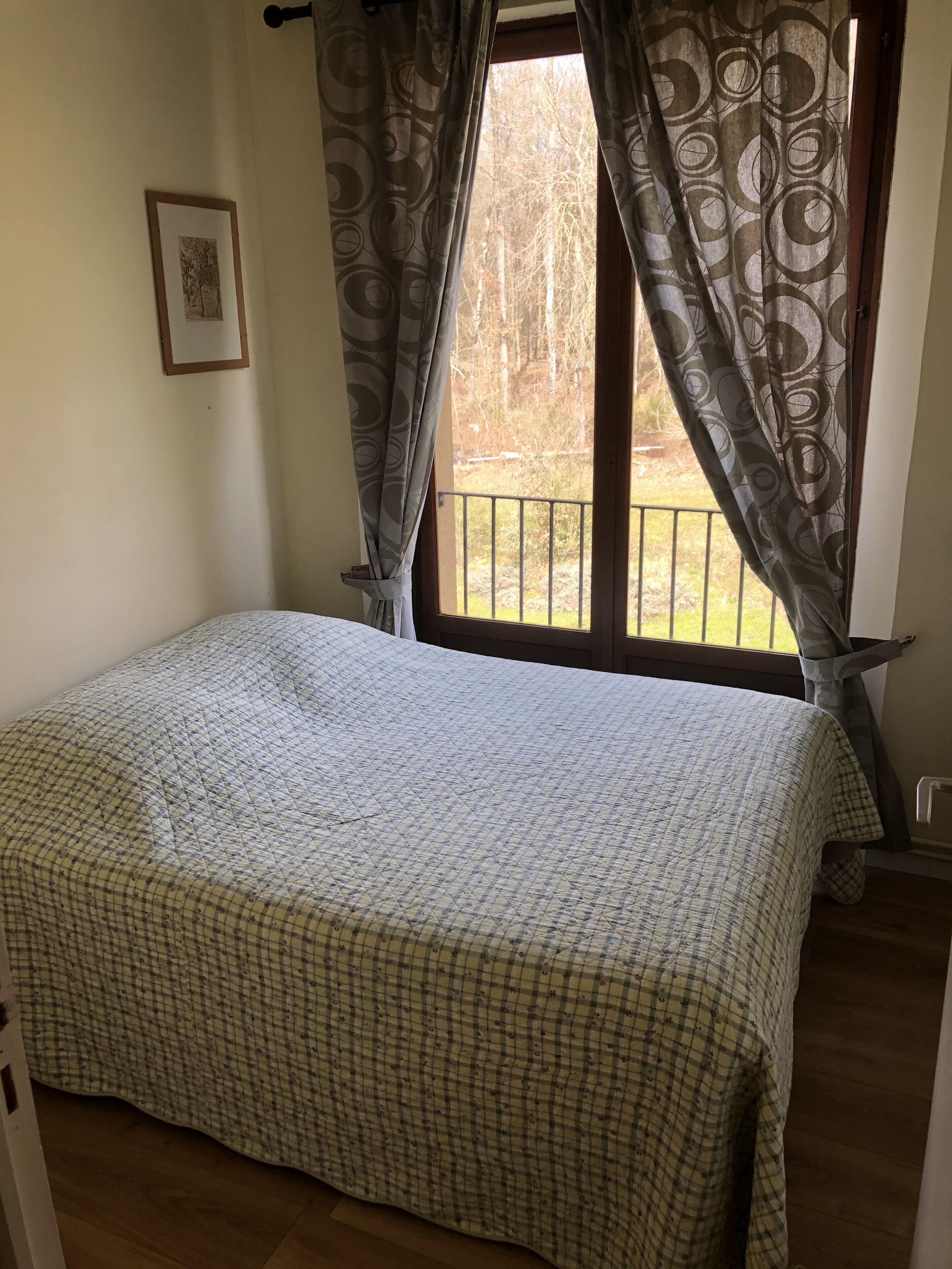 Un dormitorio con cama, ventana con cortinas, un cuadro en la pared y un balcón exterior.