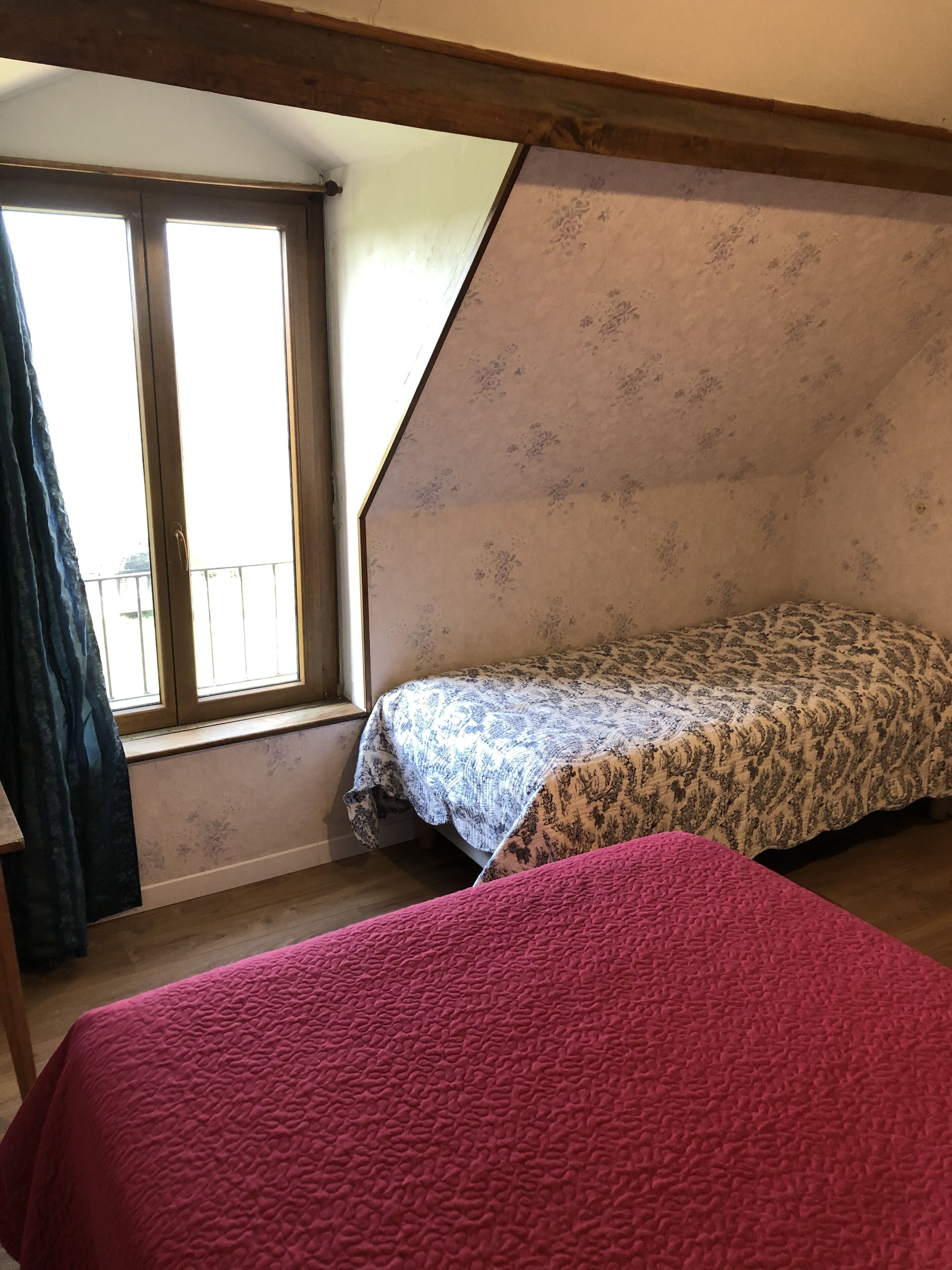 A bedroom with a sloped ceiling, a window with curtains, a bed with a patterned bedspread, and a pink blanket.
