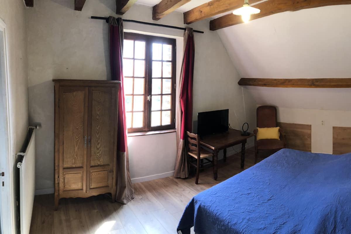 A bedroom with a bed, wooden wardrobe, desk, chair, and a window with curtains.