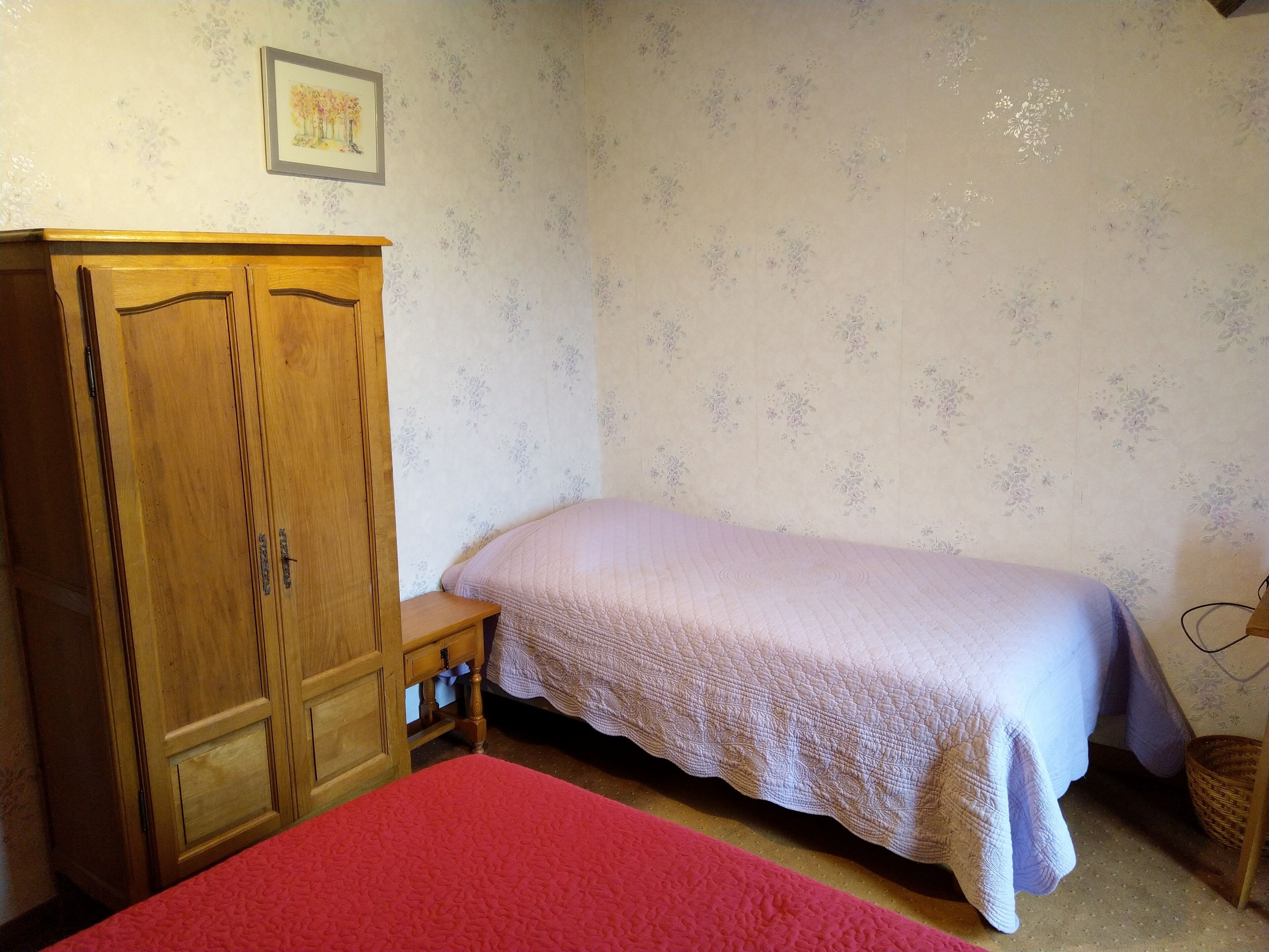 A bedroom with a bed, a wooden wardrobe, and a small bedside table.