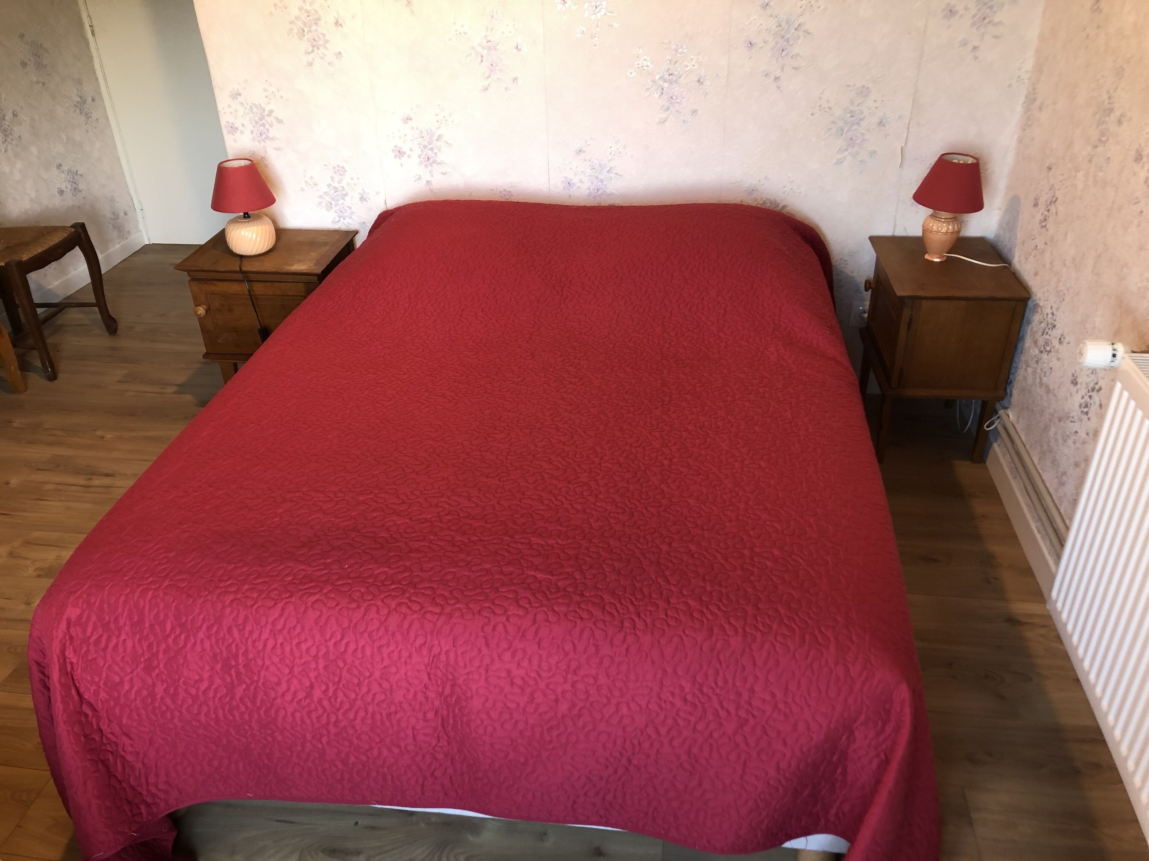 A room with a single bed, two nightstands, a chair, and a radiator.