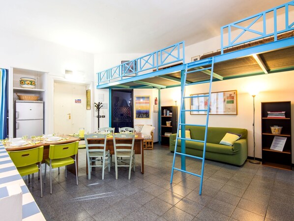 A compact living space with a dining area, a sofa, a ladder, and a bookshelf.