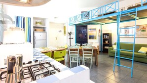 A compact kitchen with a gas stove, a dining table with chairs, and a blue loft bed structure.