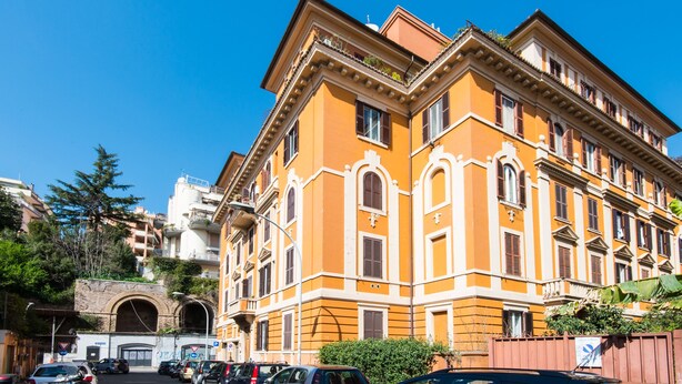 A multi-story building with a yellow facade and white trim, featuring arched windows and a central entrance.