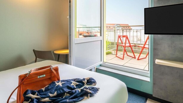Ein Hotelzimmer mit Bett, Fenster mit Außenblick, Stuhl und Fernseher.
