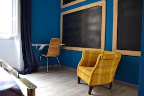 Une pièce avec un mur bleu, un bureau en bois, un fauteuil à carreaux jaunes et un tableau noir.