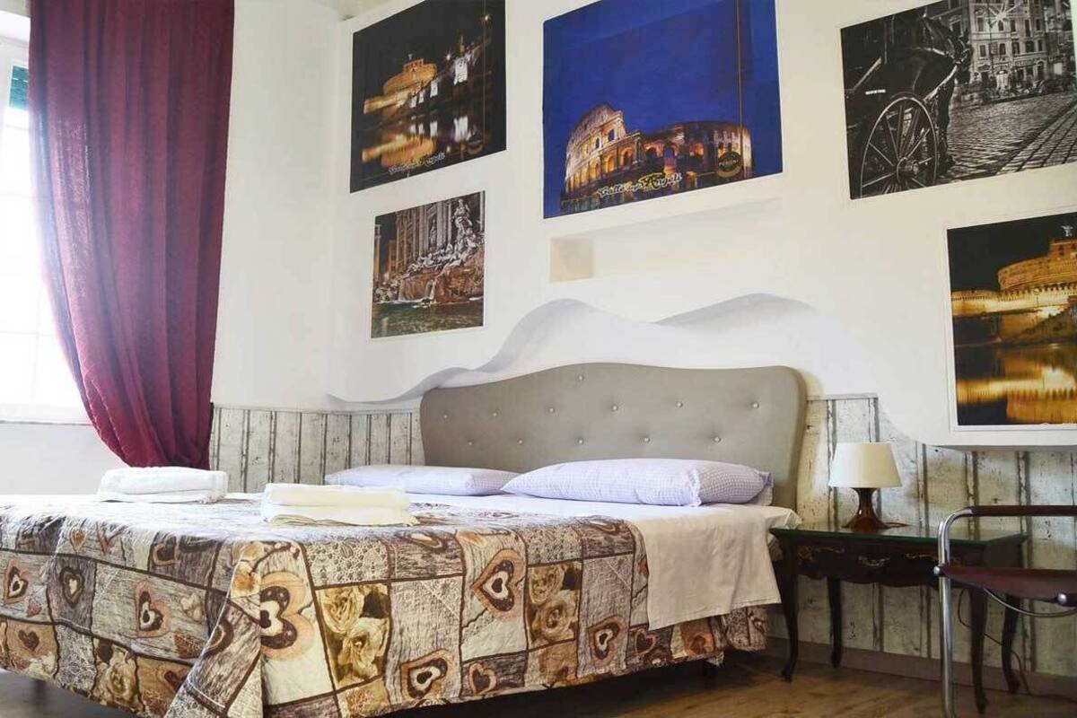 A bedroom with a bed, a nightstand, a chair, and wall art depicting historical buildings.