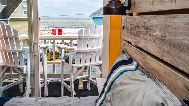 Een kamer met uitzicht op de oceaan, met een bed, een houten hoofdbord en een tafel met stoelen.