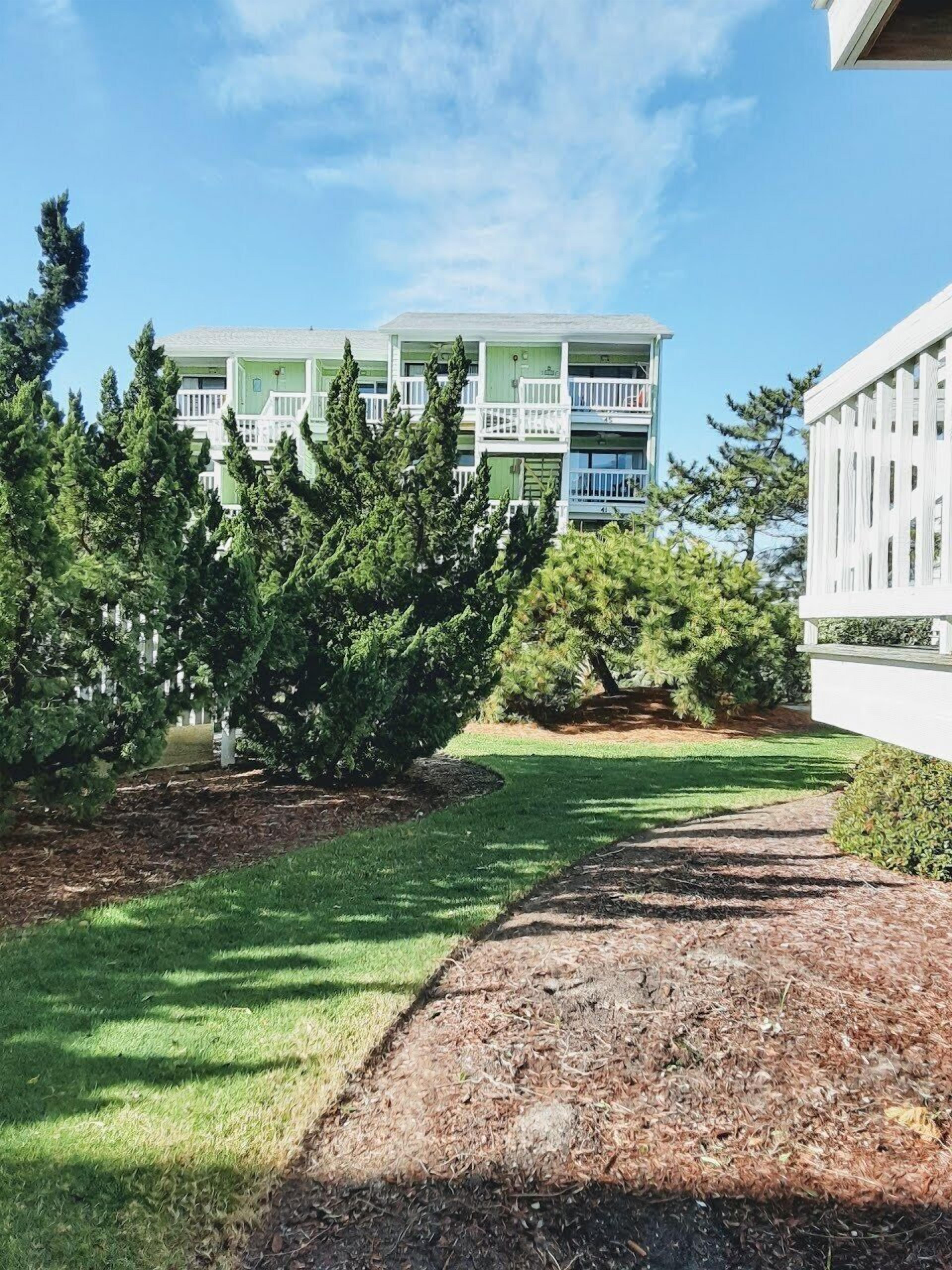 A building with a green facade and white balconies, surrounded by trees and a grassy area.