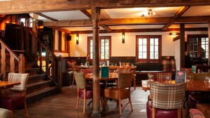Un restaurante acogedor con vigas de madera, una escalera y una mezcla de sillas de madera y tapizadas.
