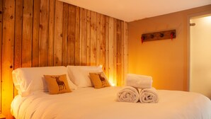 Una cama bien tendida con sábanas blancas, dos almohadas con diseños de ciervo y un par de toallas enrolladas.