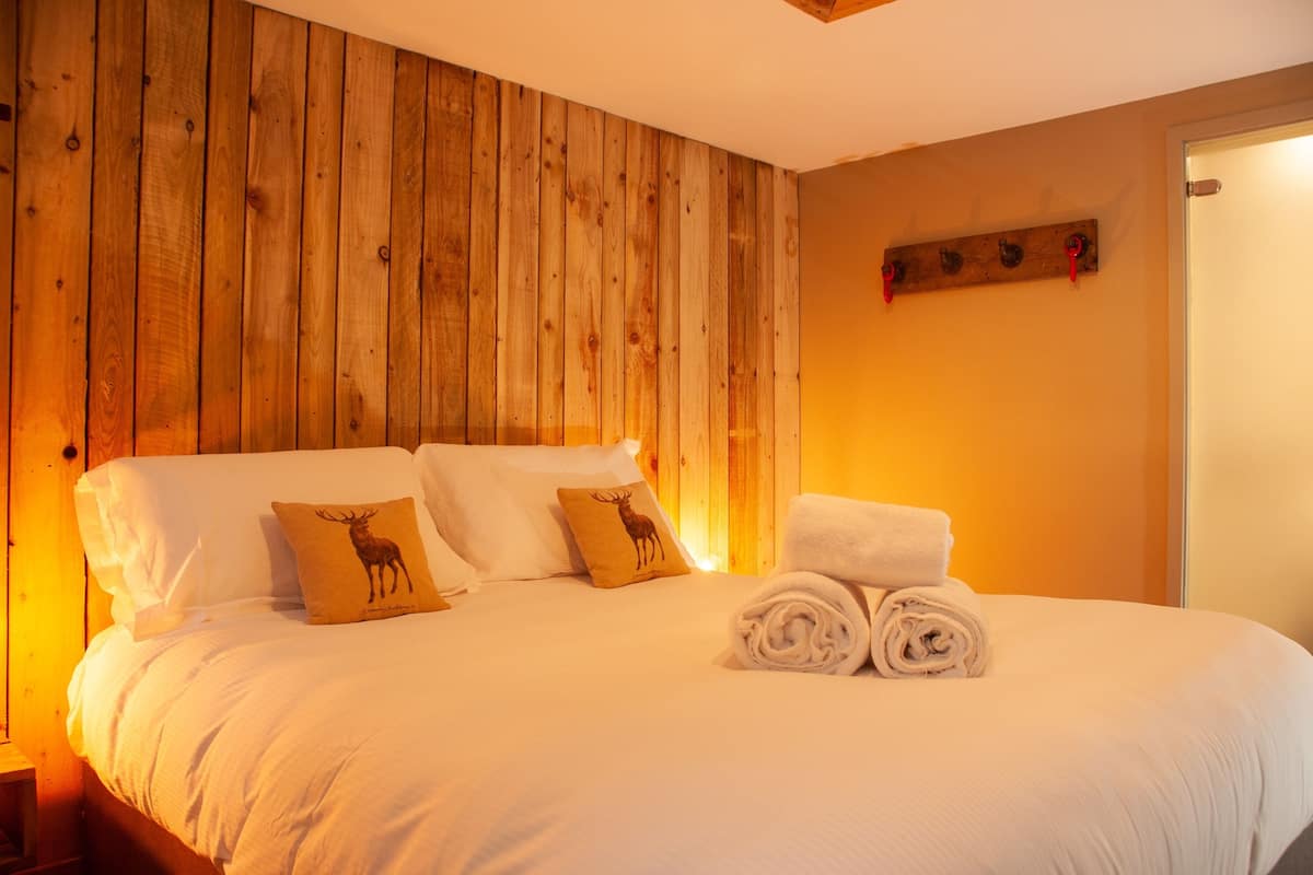 A neatly made bed with white linens, two pillows with deer designs, and a pair of rolled towels.