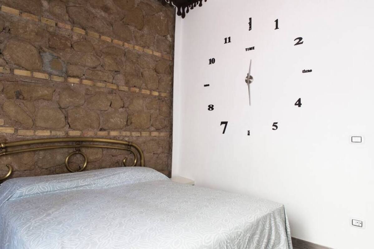 A bedroom with a brick wall, a metal bed frame, and a wall clock.