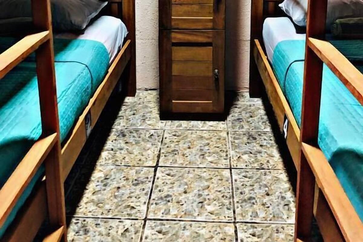 Une chambre de dortoir avec des lits superposés, une porte en bois et un sol carrelé.