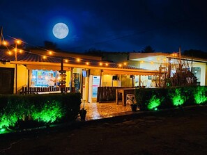 A restaurant with outdoor seating, a visible menu board, and a full moon in the background. - Hostel Ilha do Amor (Fernando de Noronha)
