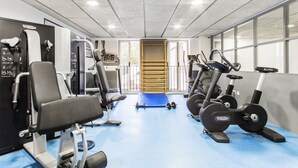 Un gimnasio con máquinas de cardio, equipo de levantamiento de pesas y una colchoneta azul en el centro.