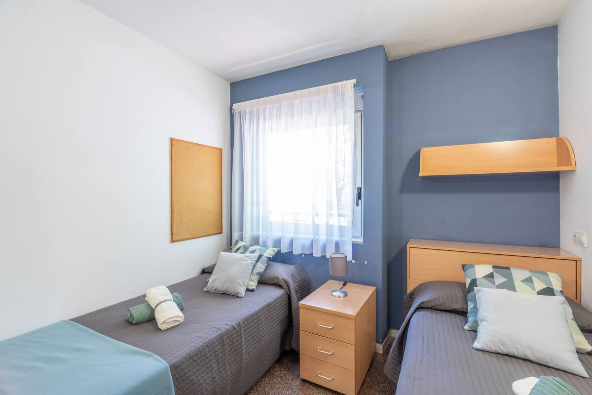 Un dormitorio con dos camas, una mesita de noche, una lámpara y una ventana con cortinas.