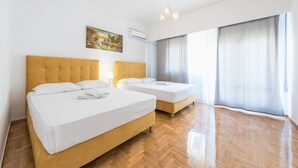 Habitación de hotel con dos camas, piso de madera, un cuadro en la pared y un ventanal con cortinas.