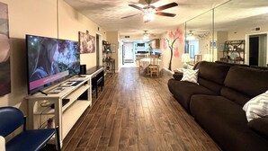 A living room with a TV, wooden flooring, a ceiling fan, a couch, and a dining area with a table and chairs.
