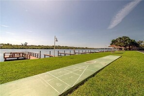A green shuffleboard court with a wooden deck and a view of a lake and distant buildings.