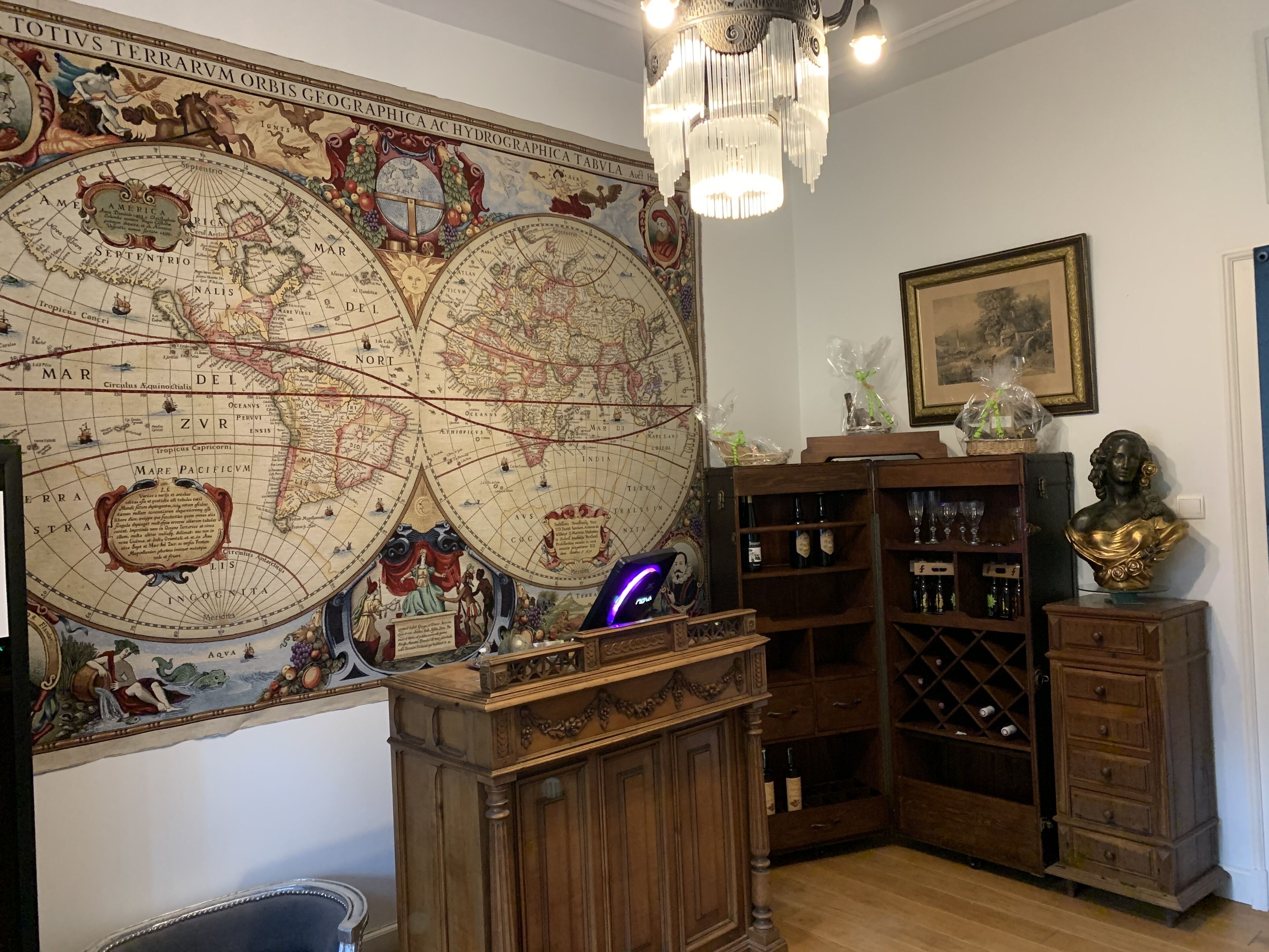 Una habitación con un gran mapa antiguo en la pared, muebles de madera y una araña.