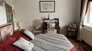 A bedroom with a large bed, a wooden dresser, a chair, a framed picture on the wall, and a window with curtains.