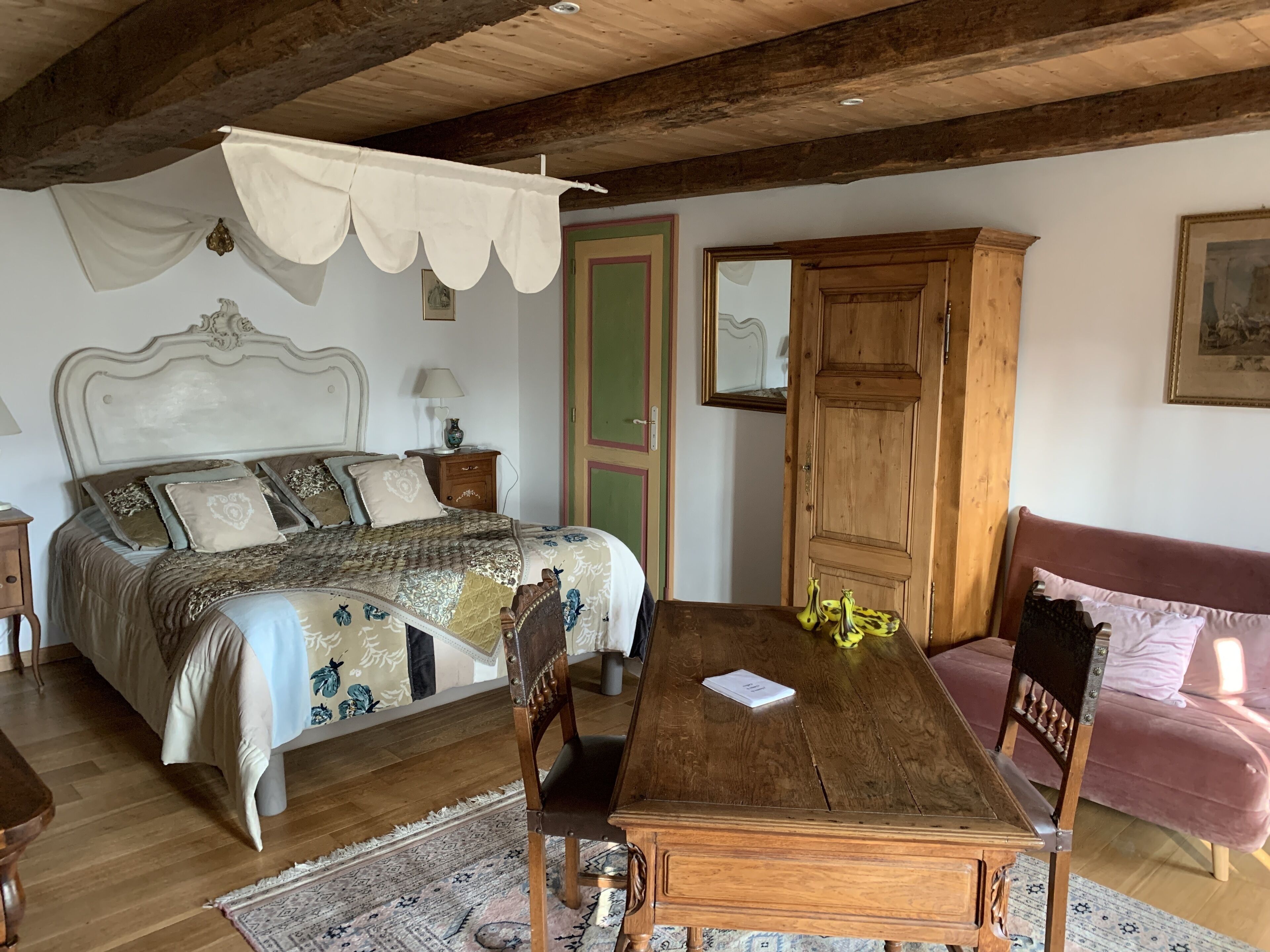 A bedroom with a wooden bed, a wooden nightstand, a wooden dresser, a wooden dining table with chairs, and a pink sofa.