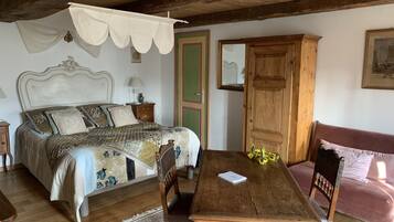 A bedroom with a wooden bed, a wooden nightstand, a wooden dresser, a wooden dining table with chairs, and a pink sofa.