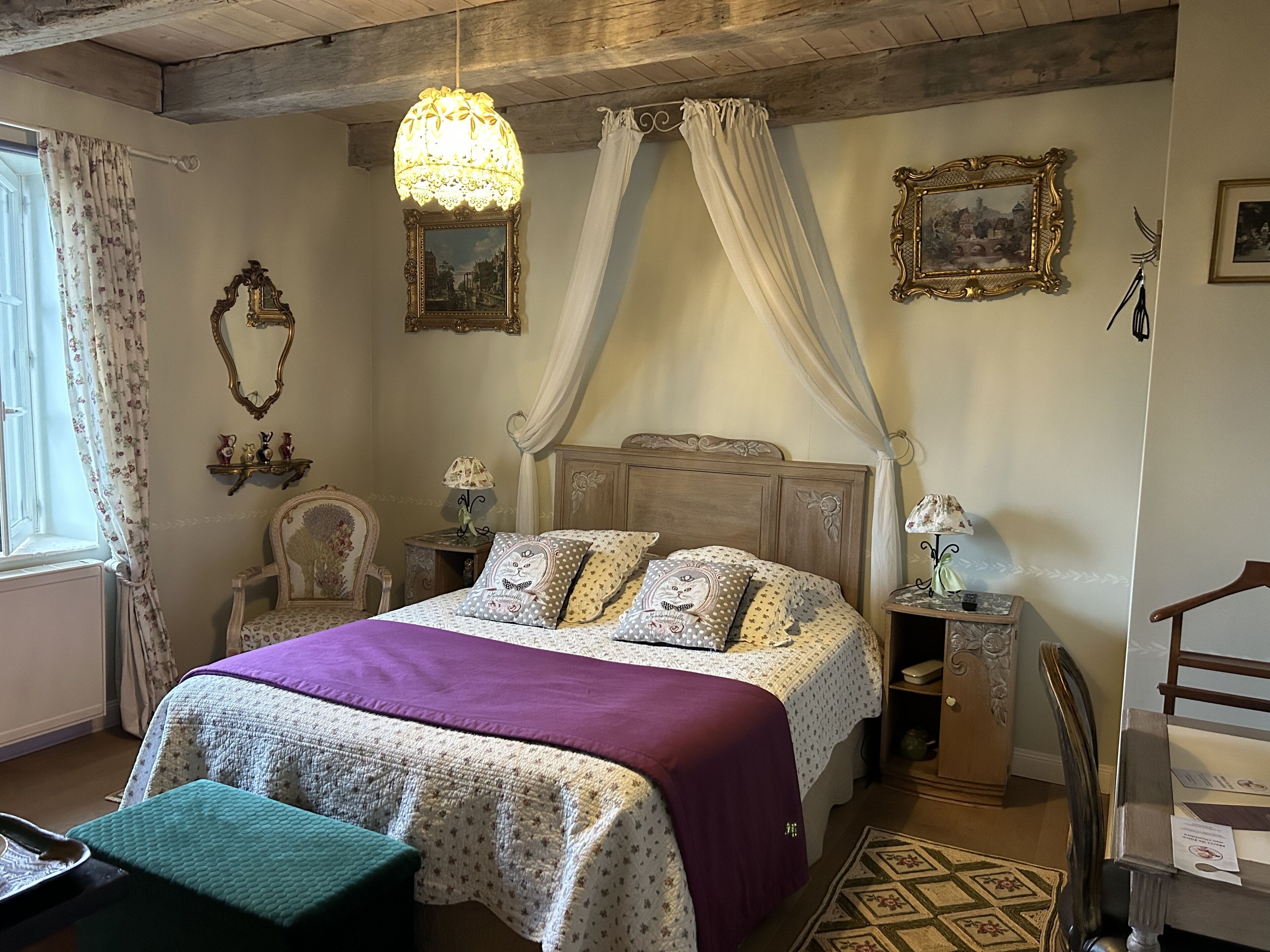 A bedroom with a wooden bed, a canopy, a nightstand, a chair, and a window with curtains.