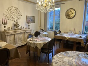 Comedor con candelabros ornamentales, un gran reloj de pared y vistas al exterior a través de una ventana.