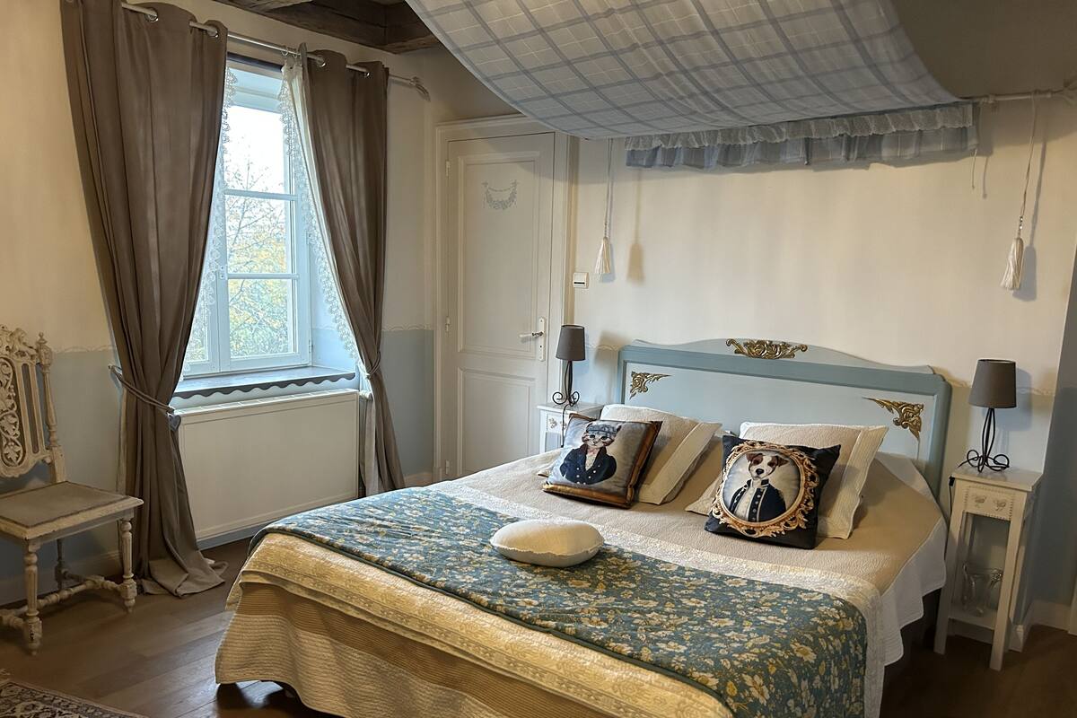 Un dormitorio con una cama, una ventana con cortinas, una mesita de noche y una lámpara.