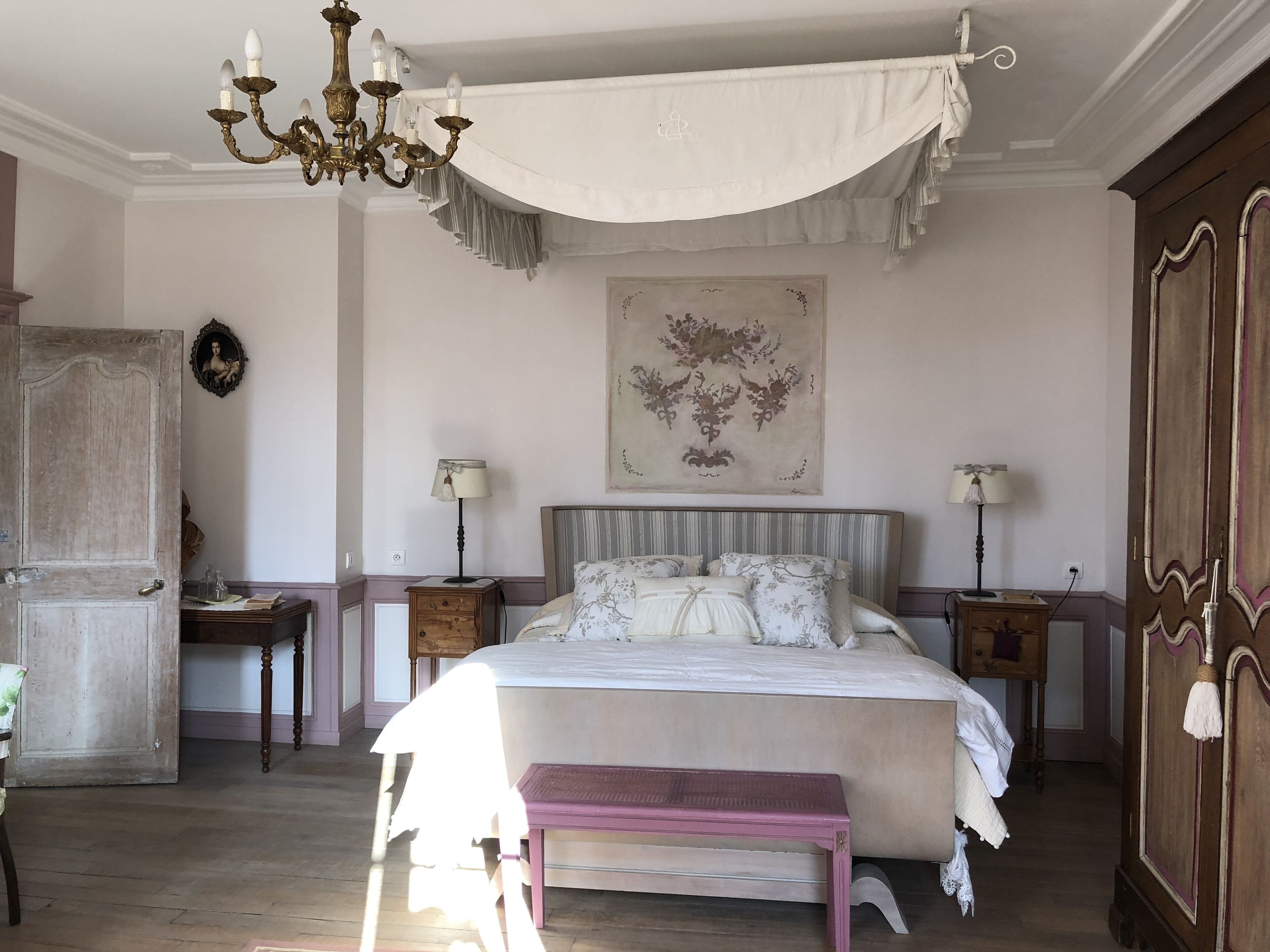 Un dormitorio con una cama grande, dos mesitas de noche, una araña, una obra de arte en la pared y un armario.