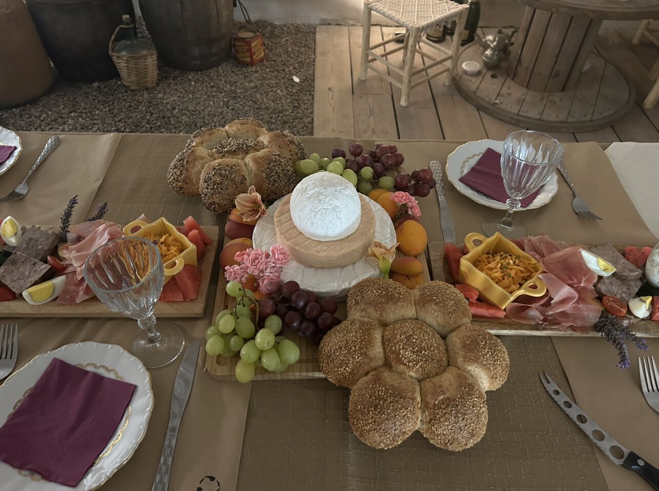 Una mesa preparada para una comida con diversos quesos, panes, frutas y embutidos.