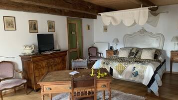 A bedroom with a wooden ceiling, a bed with patterned bedding, a desk with a chair, a television, and a green door.