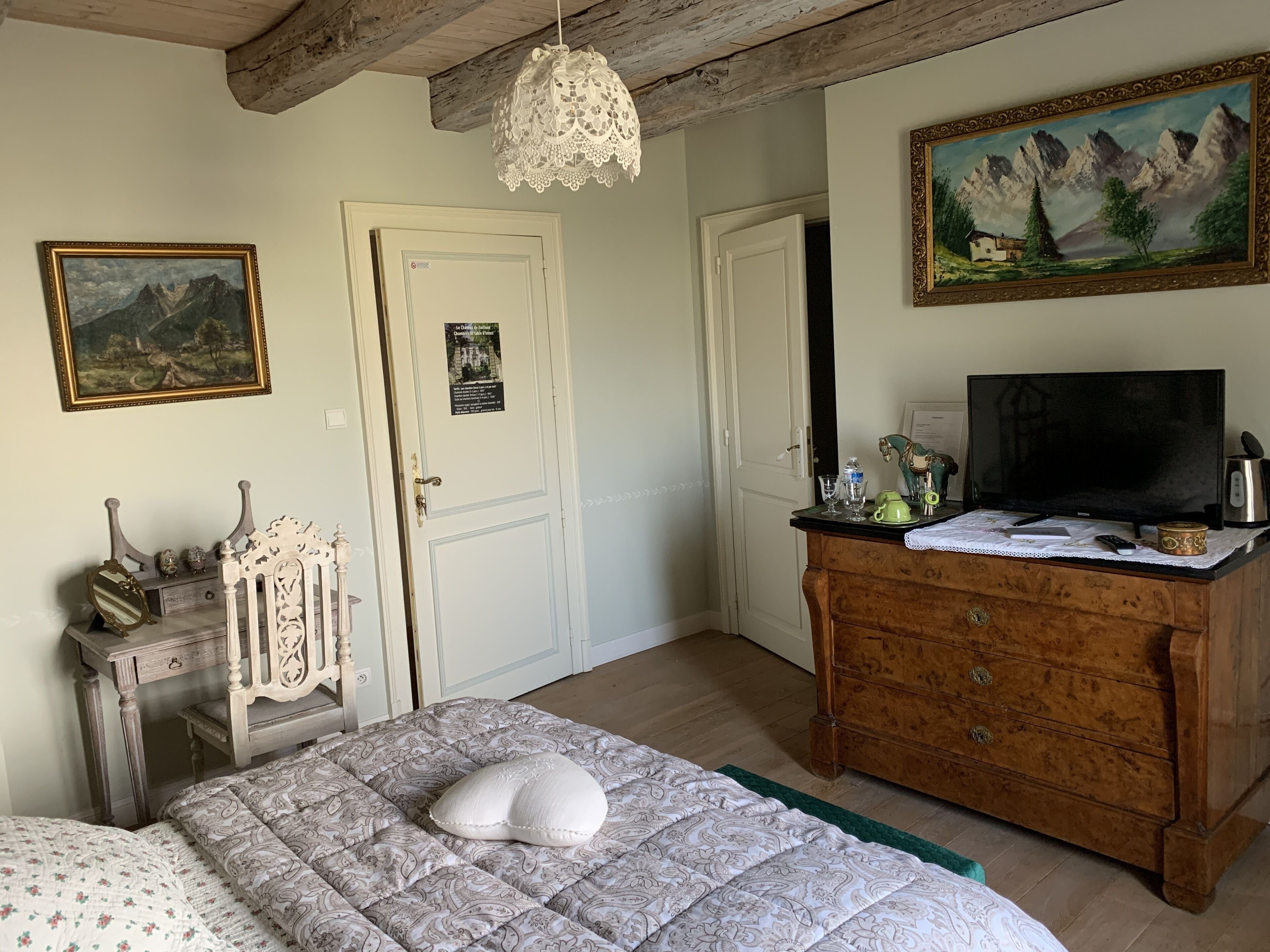 Een slaapkamer met een bed, een dressoir, een televisie en schilderijen aan de muur.