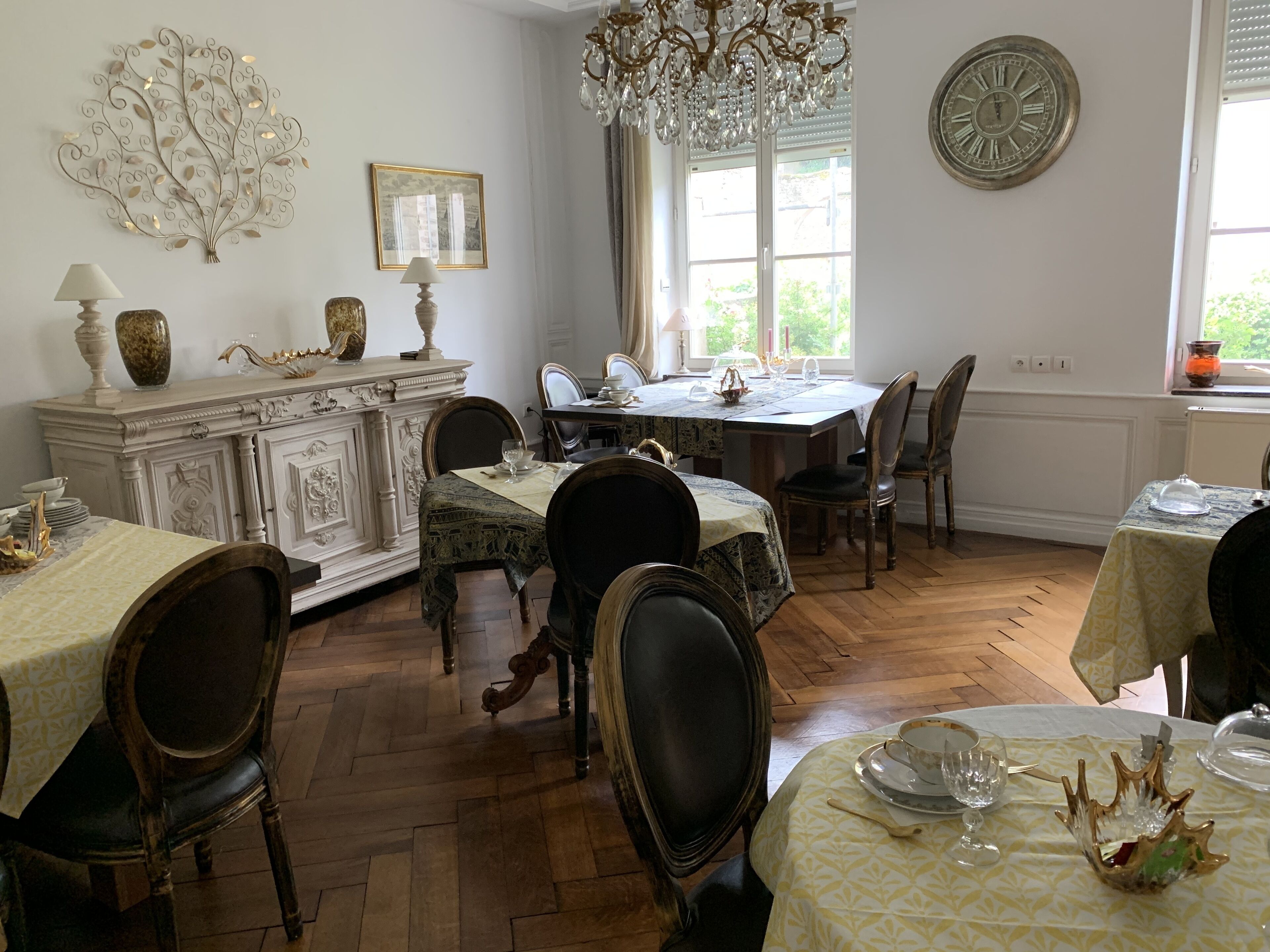 A dining area with a chandelier, a clock, and a window with curtains.