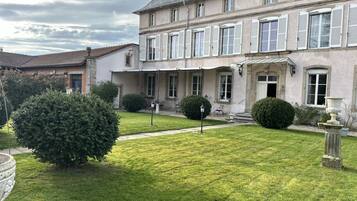 A two-story building with a well-maintained lawn, a large bush, and a stone fountain.