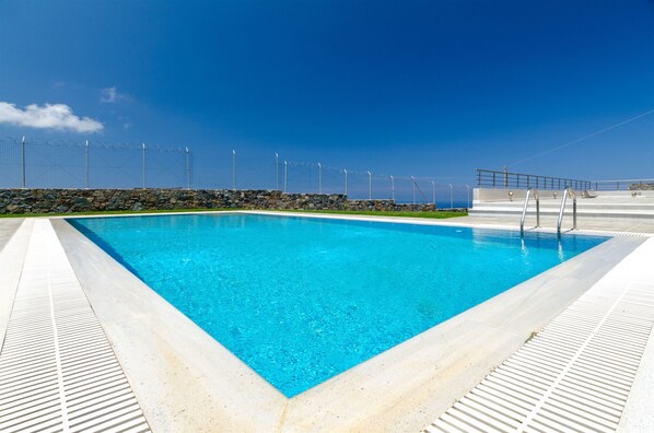A rectangular pool with clear blue water, surrounded by a stone wall and metal railing.