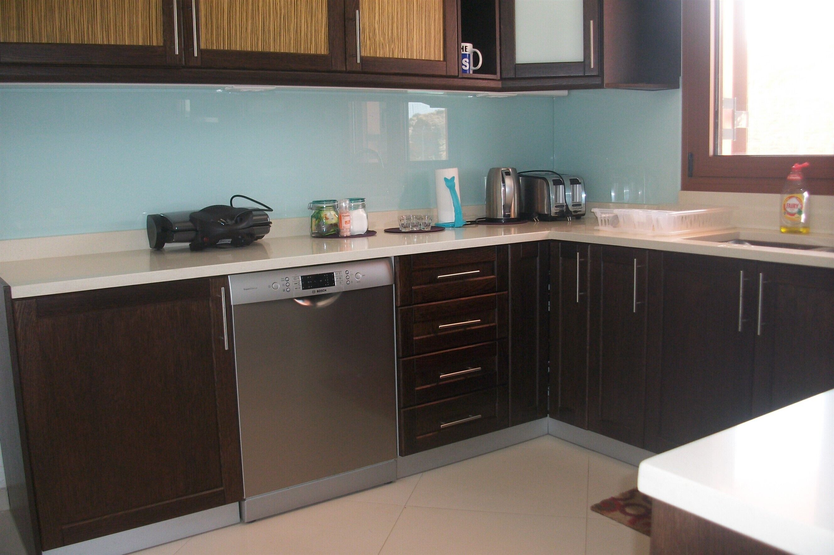A kitchen with dark wooden cabinets, a dishwasher, a coffee maker, and a window with a view.