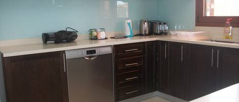 A kitchen with dark wooden cabinets, a dishwasher, a coffee maker, and a window with a view.