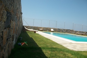 Una piscina con sillas de descanso y un muro de piedra.