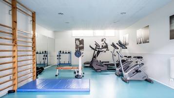 A gym with exercise equipment, a wooden climbing wall, and a blue padded floor.