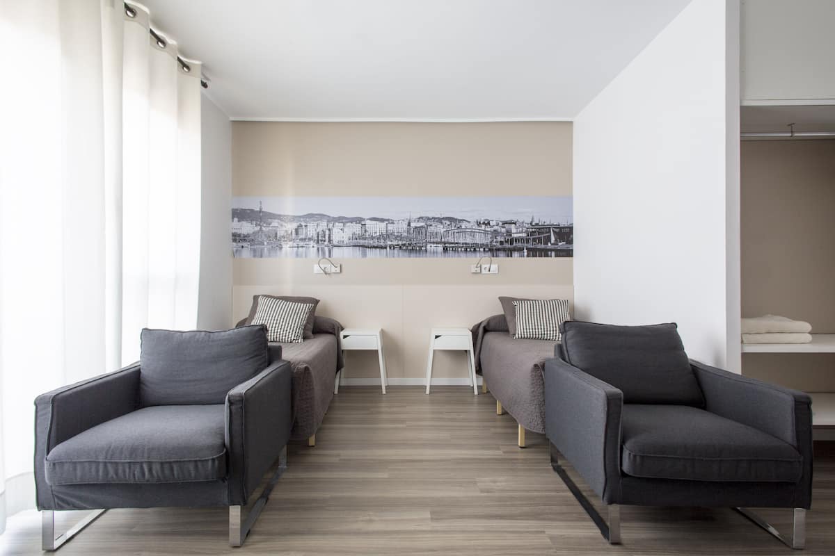 Een moderne kamer met twee grijze fauteuils, een witte bijzettafel en een groot stadsgezichtschilderij aan de muur.