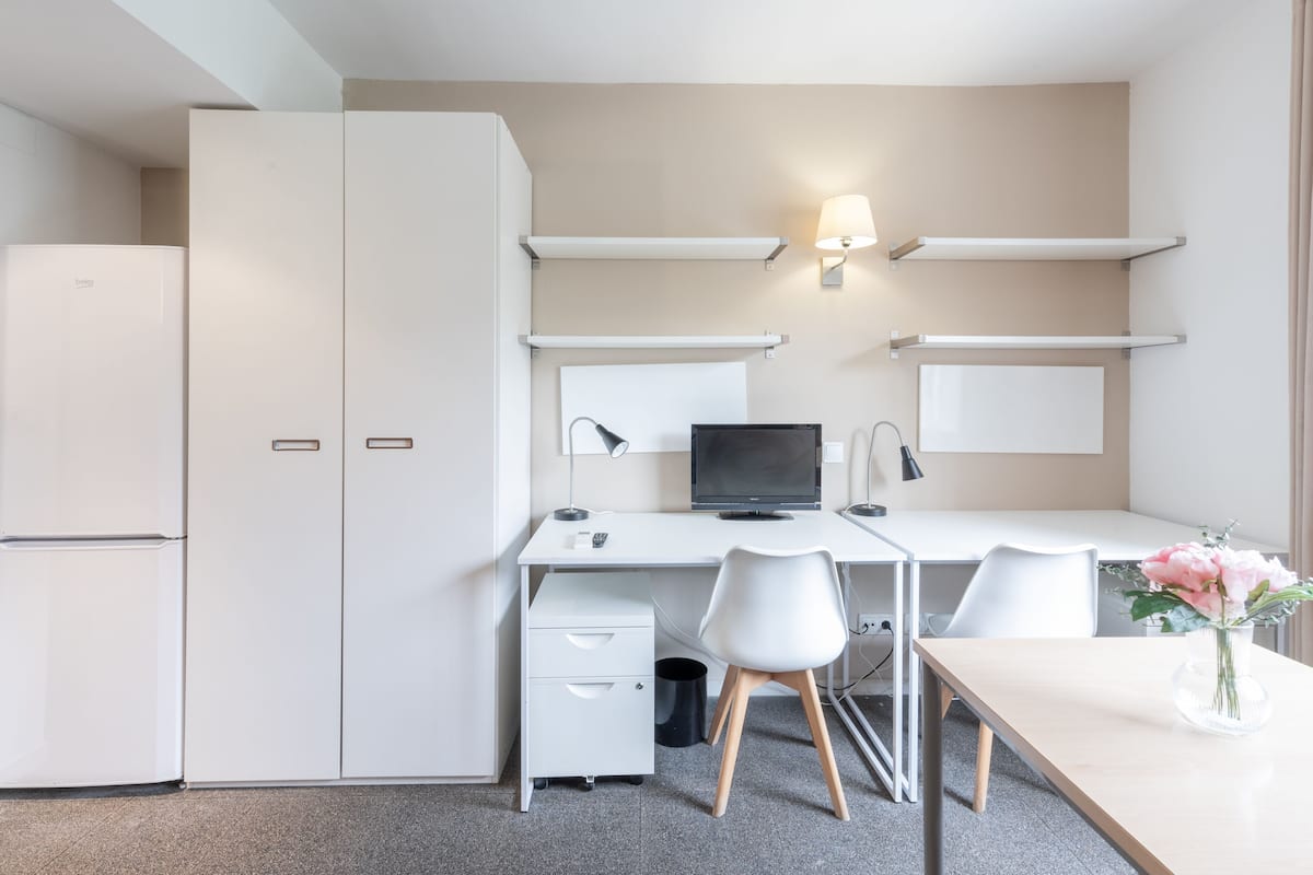 Een moderne, minimalistisch ingerichte kamer met een wit bureau, twee stoelen, een computer en een kleine prullenbak.