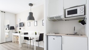 Een moderne keuken met witte kasten, een ingebouwde magnetron, een vaatwasser en een spoelbak. Er is een eethoek met een witte tafel en zwarte stoelen.