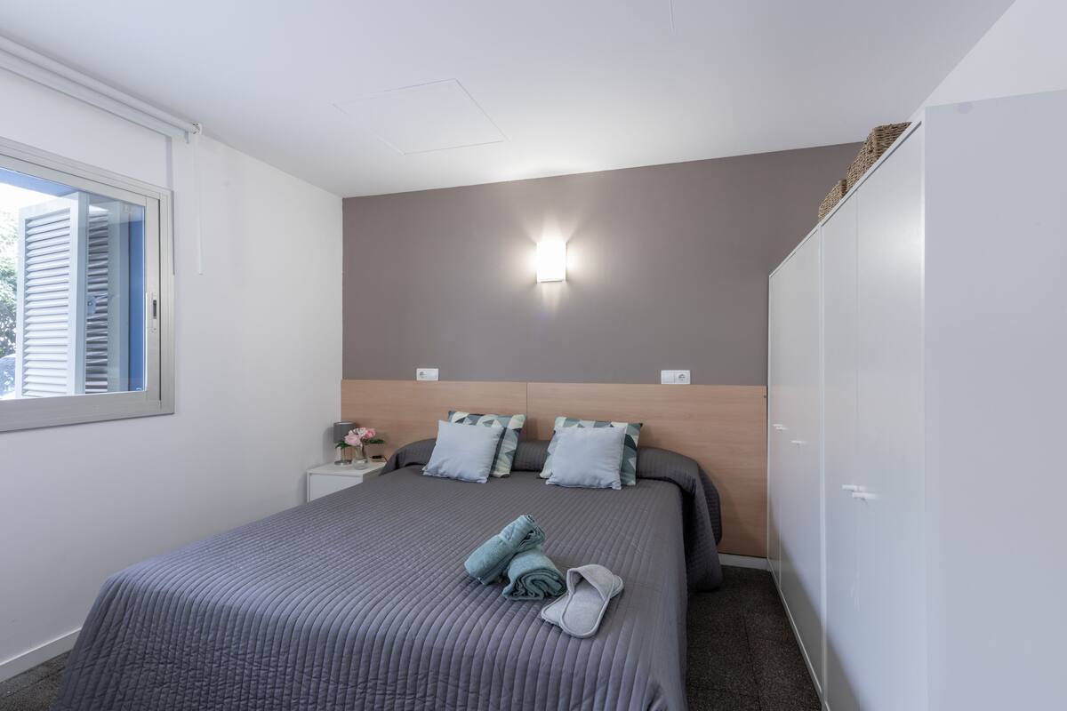 Een slaapkamer met een bed, nachtkastje, een wandlamp en een kledingkast.