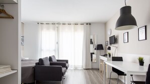 Een moderne hotelkamer met een bed, twee sofa's, een bureau en een groot raam met gordijnen.