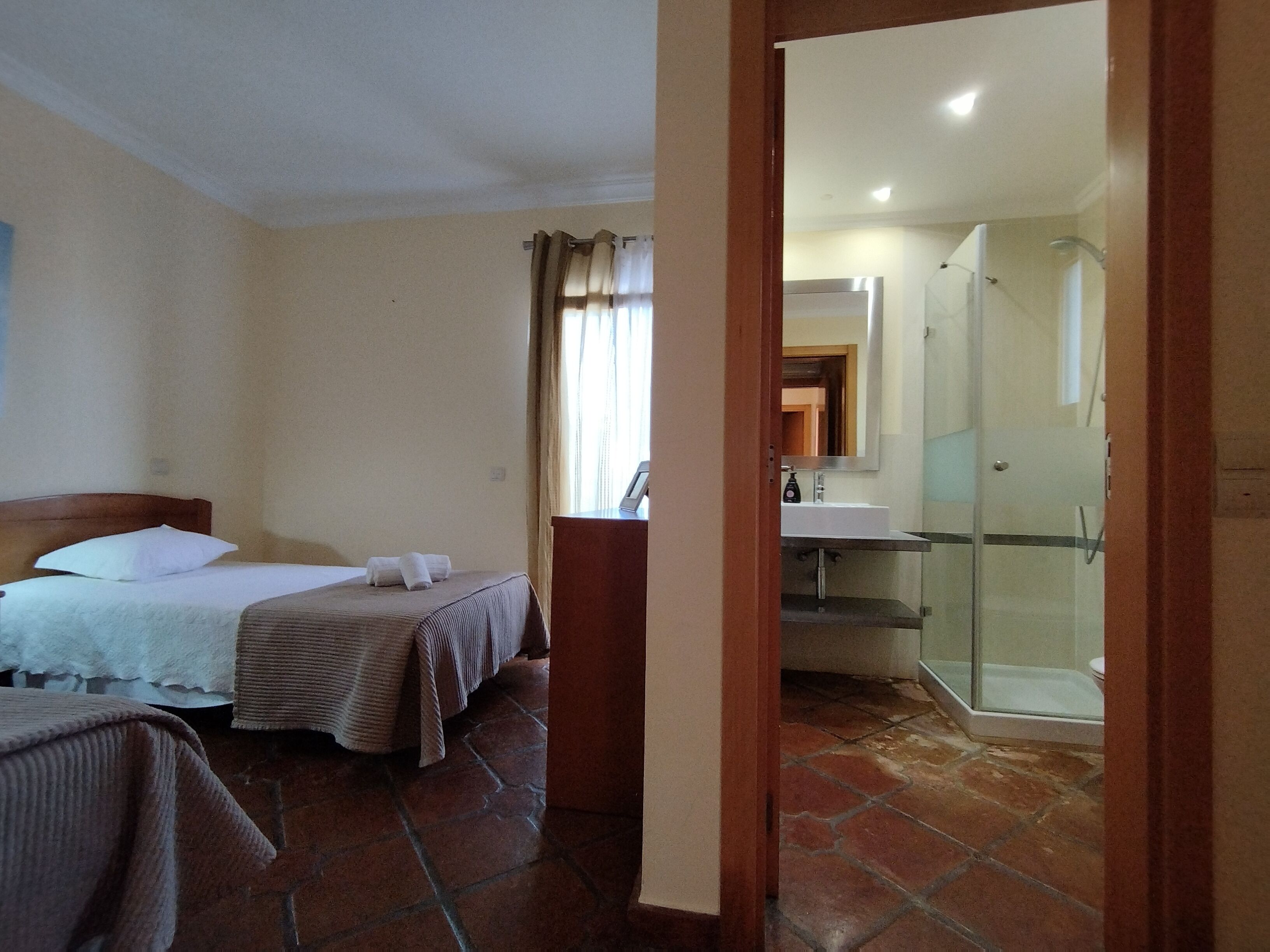 Una habitación de hotel con cama, mesita de noche, baño con ducha y lavamanos.
