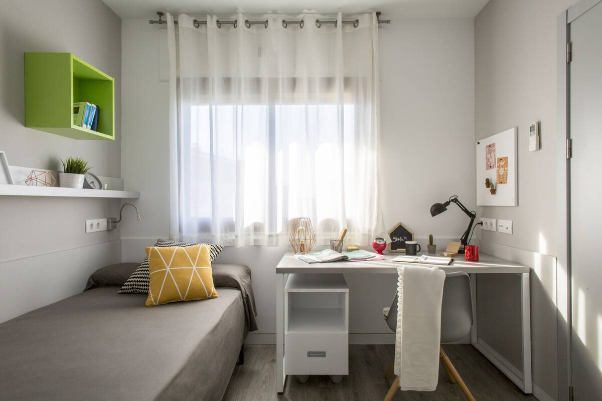 A compact bedroom with a bed, a desk, and a green shelf.